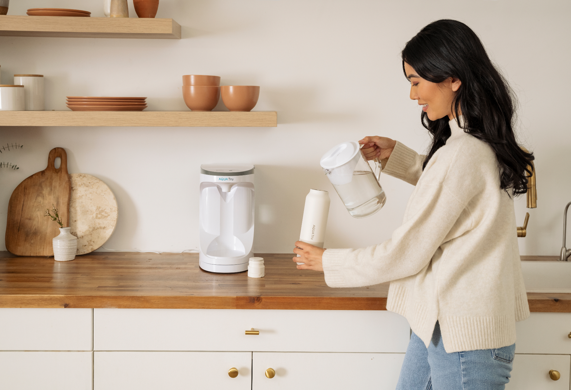 Pouring purified water from the AquaTru Carafe into a bottle in a bright kitchen